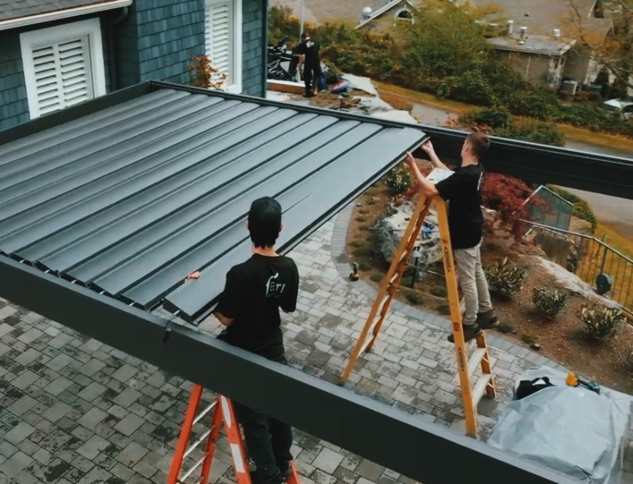 Workers installing a Pergolux pergola - two installers on ladders fitting louvered roof panels